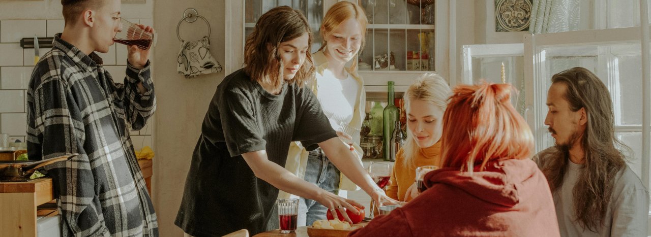 A group of young people from different countries enjoying community life in the kitchen sharing food and drink.