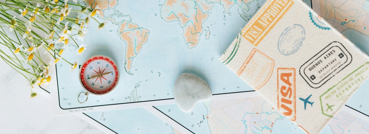 A top down photo of a compass, flowers, heart and visa or passport, representing the process of visa application to study at All Nations.